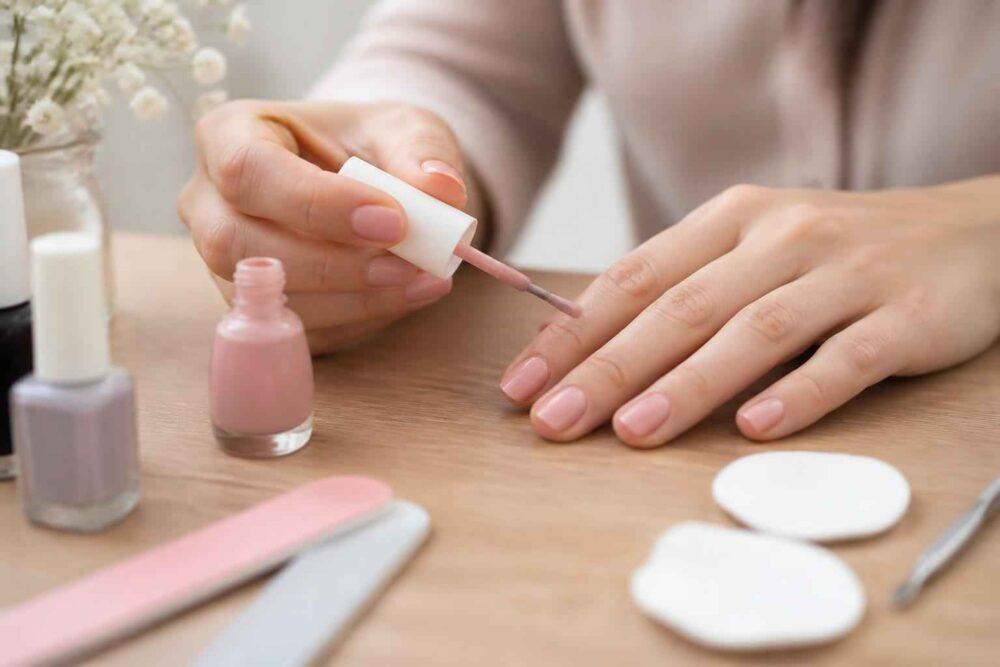Kobieta maluje paznokcie różowym lakierem przy domowym stanowisku do manicure