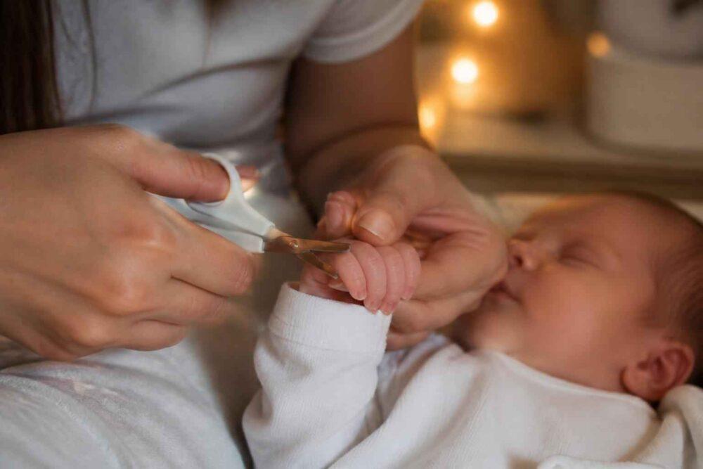 Opiekunka przycina paznokcie śpiącemu niemowlęciu w białym ubranku