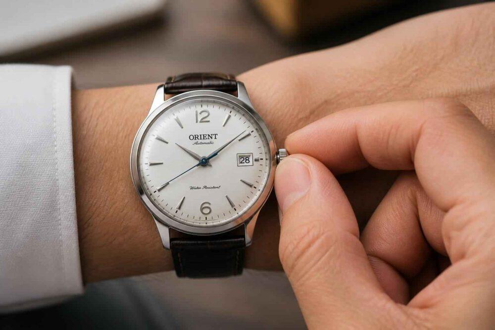 Mężczyzna reguluje koronkę eleganckiego zegarka Orient na nadgarstku