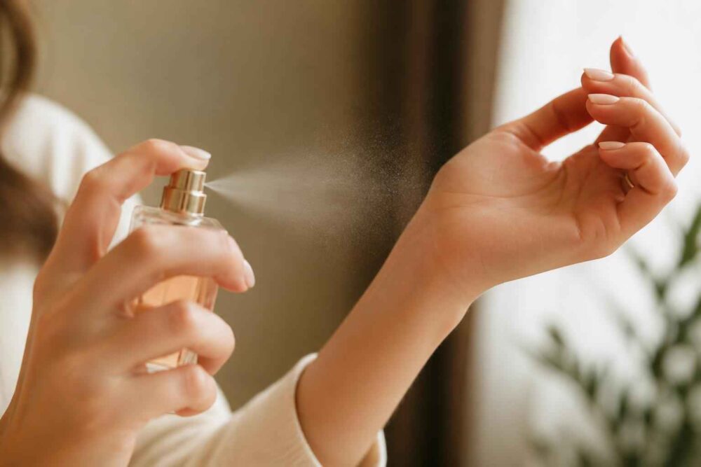 Kobieta rozpyla perfumy na nadgarstek w domowym wnętrzu